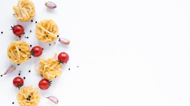 Uncooked tagliatelle pasta; cherry tomato; garlic clove; black pepper isolated over white background with space for text