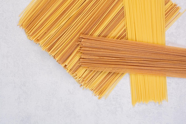 Uncooked yellow and brown spaghetti on marble table.