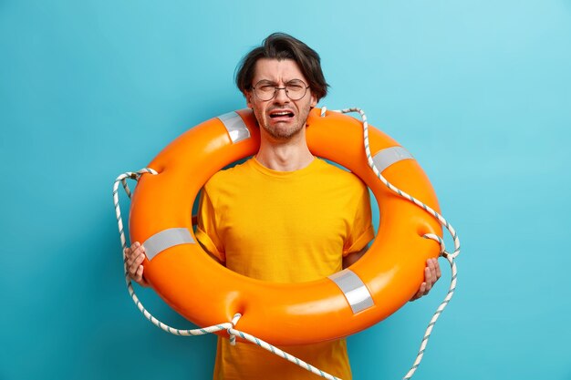 Unhappy Caucasian man learns to swim poses with lifebuoy prepares for cruise trip