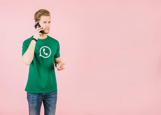 Free photo unhappy young man talking on mobile phone against pink background