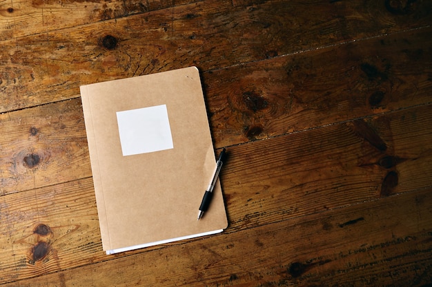 Unlabeled craft notebook and a plastic black pen on an old textured wooden table