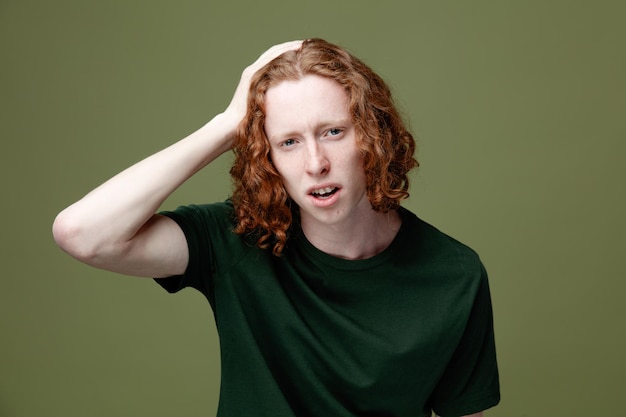 unpleased grabbed head young handsome guy wearing green t shirt isolated on green background