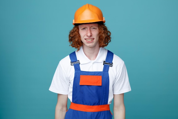 Free Photo unpleased looking at camera young builder man in uniform isolated on blue background