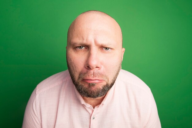 Unpleased looking middle-aged bald man wearing pink t-shirt