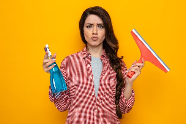 Unpleased pretty caucasian cleaner woman holding squeegee and spray cleaner 