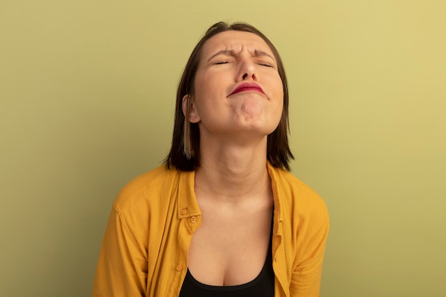 Unpleased pretty woman stands with closed eyes isolated on olive green wall