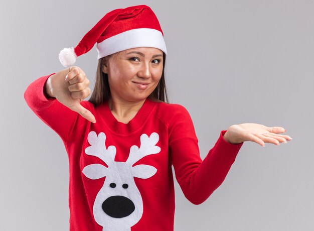 Unpleased young asian girl wearing christmas hat with sweater showing thumb down isolated on white background