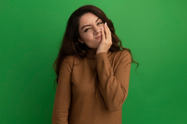 Unpleased young beautiful girl putting hand on chin isolated on green wall