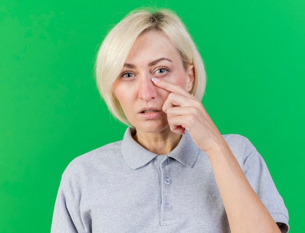 Free Photo unpleased young blonde ill slavic woman puts finger on eyelid isolated on green