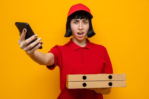 Unpleased young caucasian delivery girl holding pizza boxes and phone 