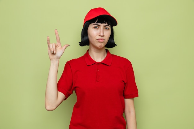 Unpleased young caucasian delivery woman gesturing horns sign 