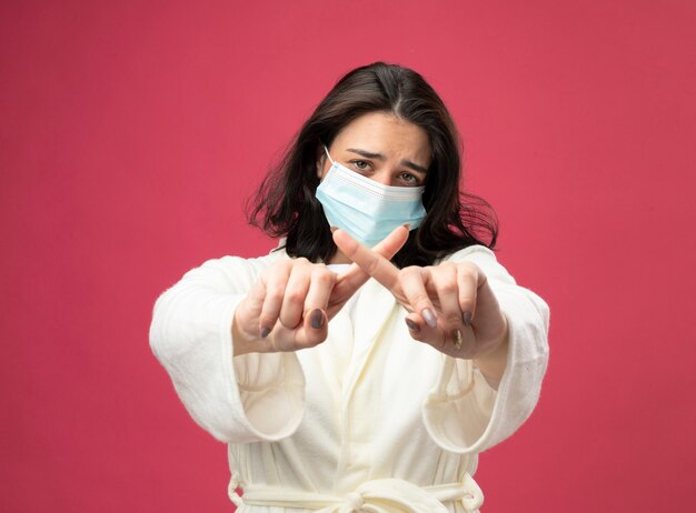 Unpleased young caucasian ill girl wearing robe and mask looking at camera doing no gesture isolated on crimson background