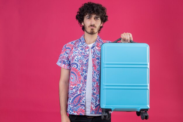 Free Photo unpleased young handsome curly traveler man holding suitcase on isolated pink wall with copy space