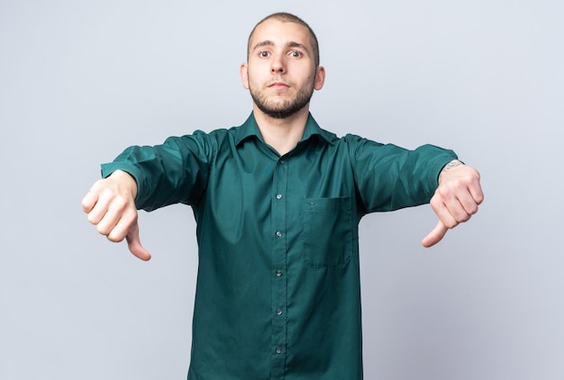 Unpleased young handsome guy wearing green shirt showing thumbs down 