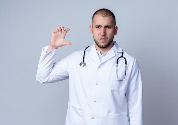 Unpleased young male doctor wearing medical robe and stethoscope around his neck showing size isolated on white background