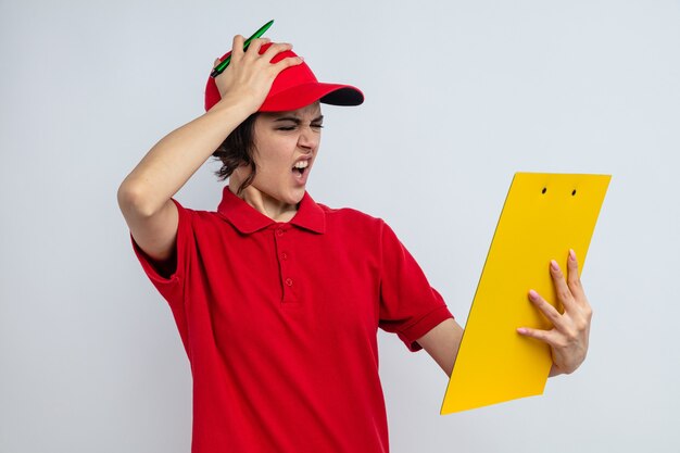 Unpleased young pretty delivery woman putting hand on her head and holding clipboard 