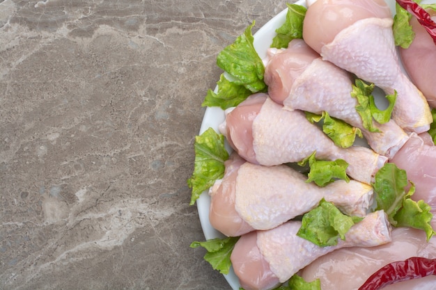 Unprepared chicken legs with lettuce on white plate