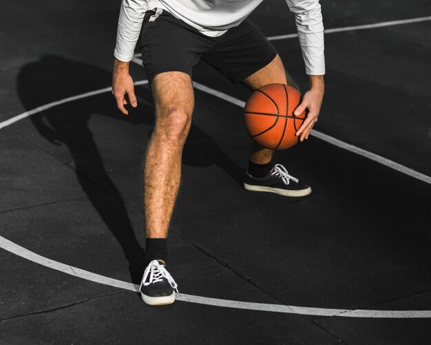 Unrecognisable man bouncing basketball on court