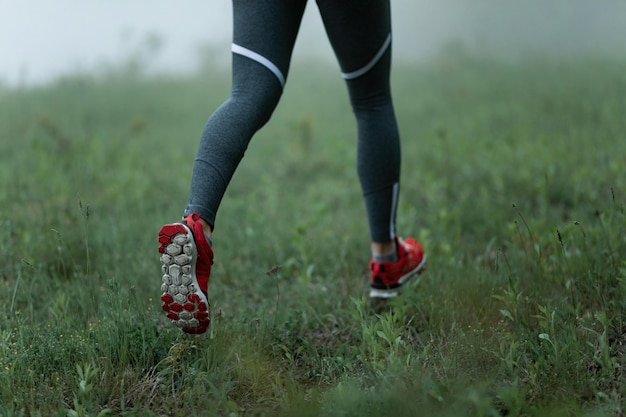 Free photo unrecognizable athletic woman running on the grass in foggy weather