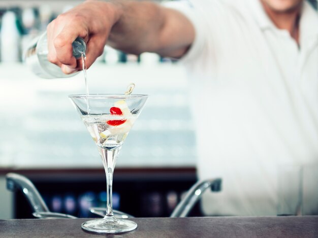 Unrecognizable barman pouring cocktail in glass