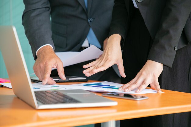 Unrecognizable businesspeople studying statistics and holding papers with hands