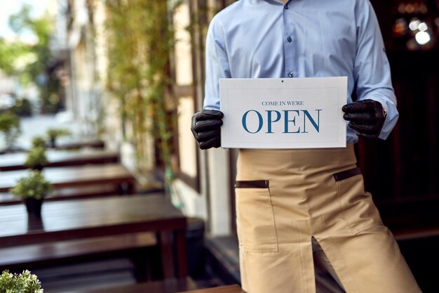 Unrecognizable coffee shop owner holding open sign while standing at the doorway