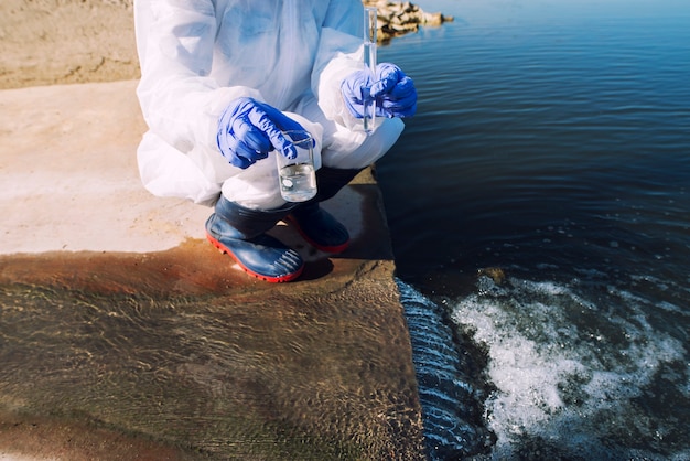 Free photo unrecognizable ecologist standing where sewage waste water meets the river and taking samples to determine level of contamination and pollution