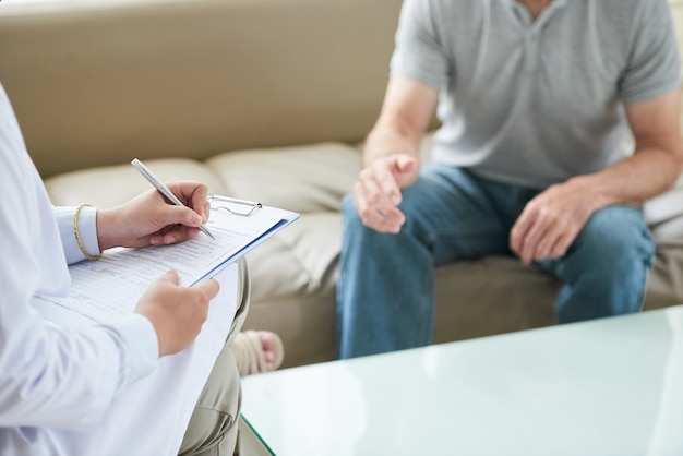 Unrecognizable female doctor talking to patient and writing during house call