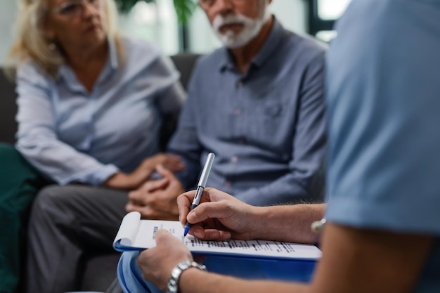 Free photo unrecognizable male doctor writing medical report while visiting senior couple at their home