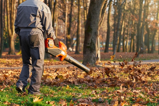 Free photo unrecognizable male worker using leaf blower in city park in fall back view of strong man wearing