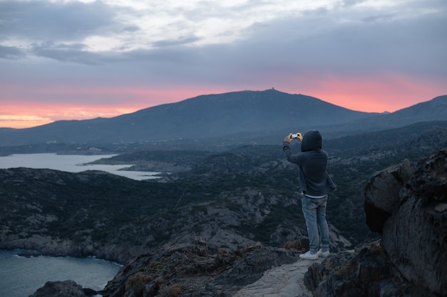 Free photo unrecognizable man in hoodie stands on top of hiking trail on mountain