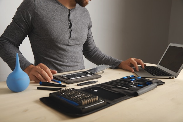 Free photo unrecognizable man looks guides in internet while repaiting his smartphone , changes screen and battery