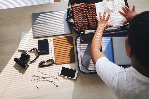 Free photo unrecognizable man packing suitcase for trip, and electronic gadgets lying nearby