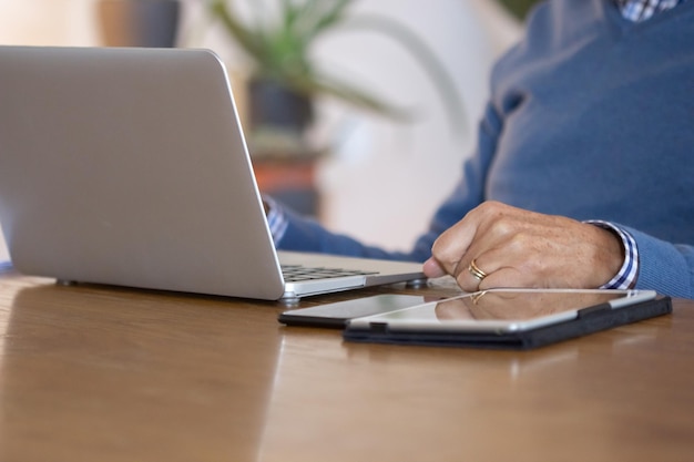 Free photo unrecognizable man using laptop while working from home. close-up shot of mature businessman looking at laptop screen, sitting at table with tablet and phone on it. digital device, workplace concept