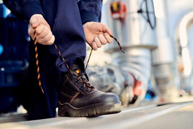 Unrecognizable manual worker typing shoelace at construction site