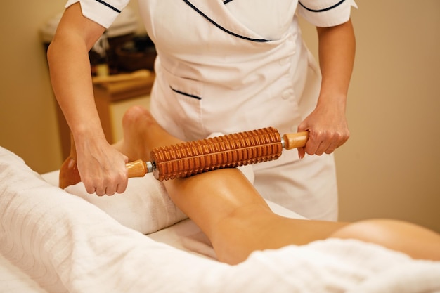 Unrecognizable therapist performing maderotherapy on woman's legs during massage treatment at the spa