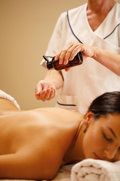 Unrecognizable therapist pouring oil in her hands before massage treatment at the wellness center