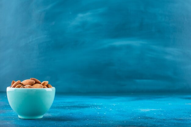 Unshelled almonds in a bowl on the blue surface