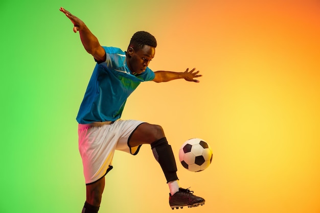 Unstoppable Africanamerican male soccer football player training in action isolated on gradient studio background in neon light Concept of motion action ahievements healthy lifestyle