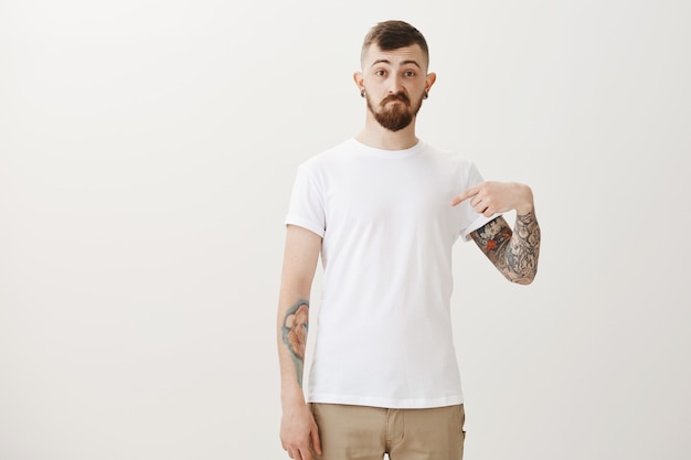 Free photo unsure hipster guy pointing finger at himself with confused expression