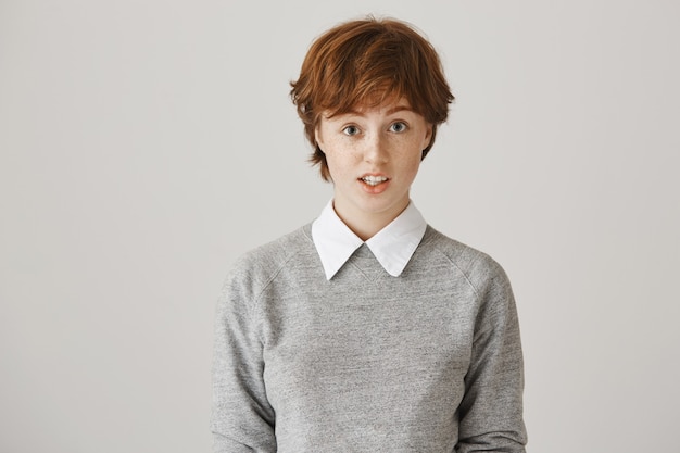 Free photo unsure redhead girl with short haircut posing against the white wall