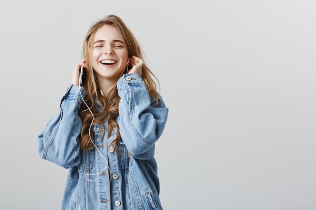 Upbeat blond girl enjoying listening music, smiling delighted