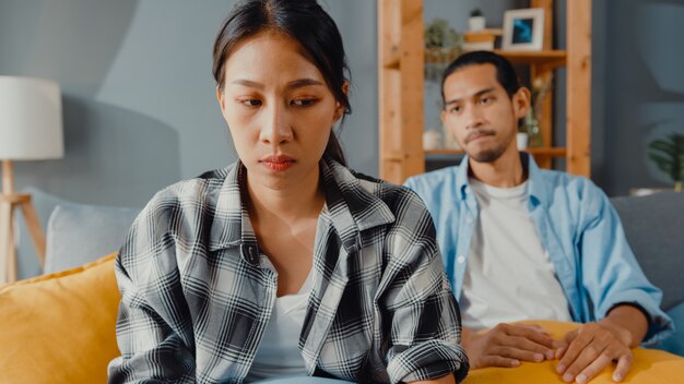 Upset asian couple sit on couch in living room