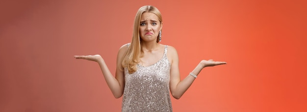 Upset clueless frustrated blond european young girl in glittering silver evening dress grimacing