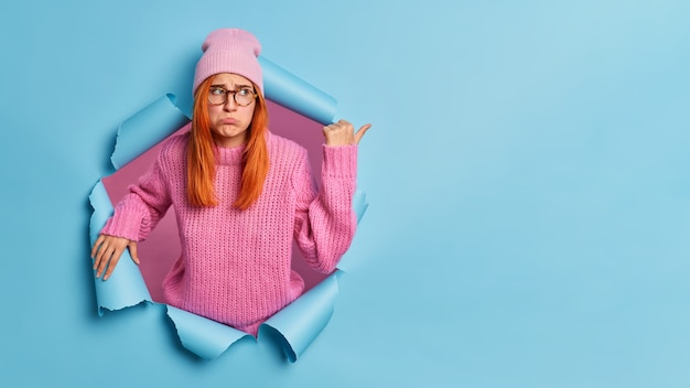 Free photo upset dejected woman with red hair being in low spirit pointing at copy space with dissatisfied expression