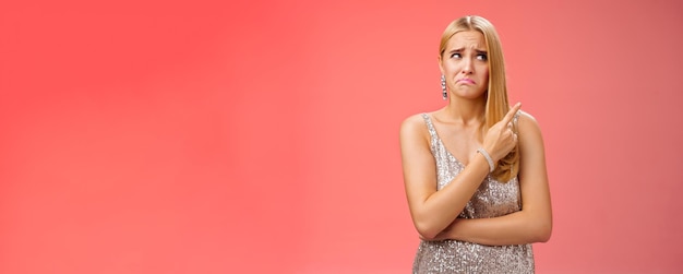 Free Photo upset doubtful unsure cute blond funny glamour girl in silver evening dress cringing grimacing hesit