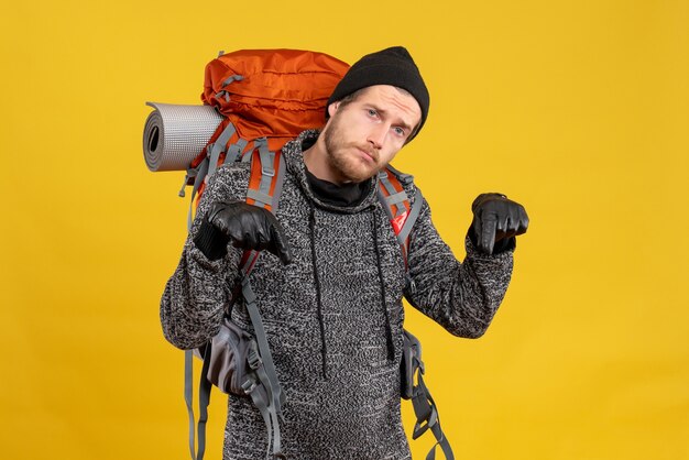 Free photo upset male hitchhiker with leather gloves and backpack pointing at floor