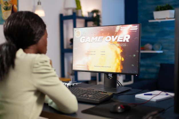 Upset pro gamer woman playing space shooter videogames losing online championship. Nervous african american player using RGB computer equipment sitting in gaming home studio. Esports tournament