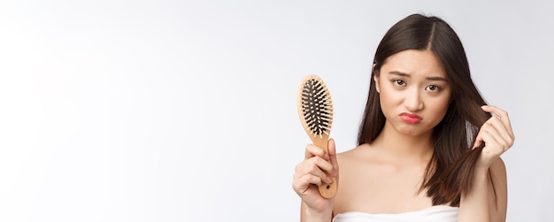 Free photo upset stressed young asian woman holding damaged dry hair on hands over white isolated background