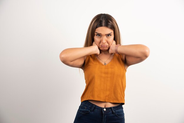 Upset woman putting hands on her neck and posing on white background.